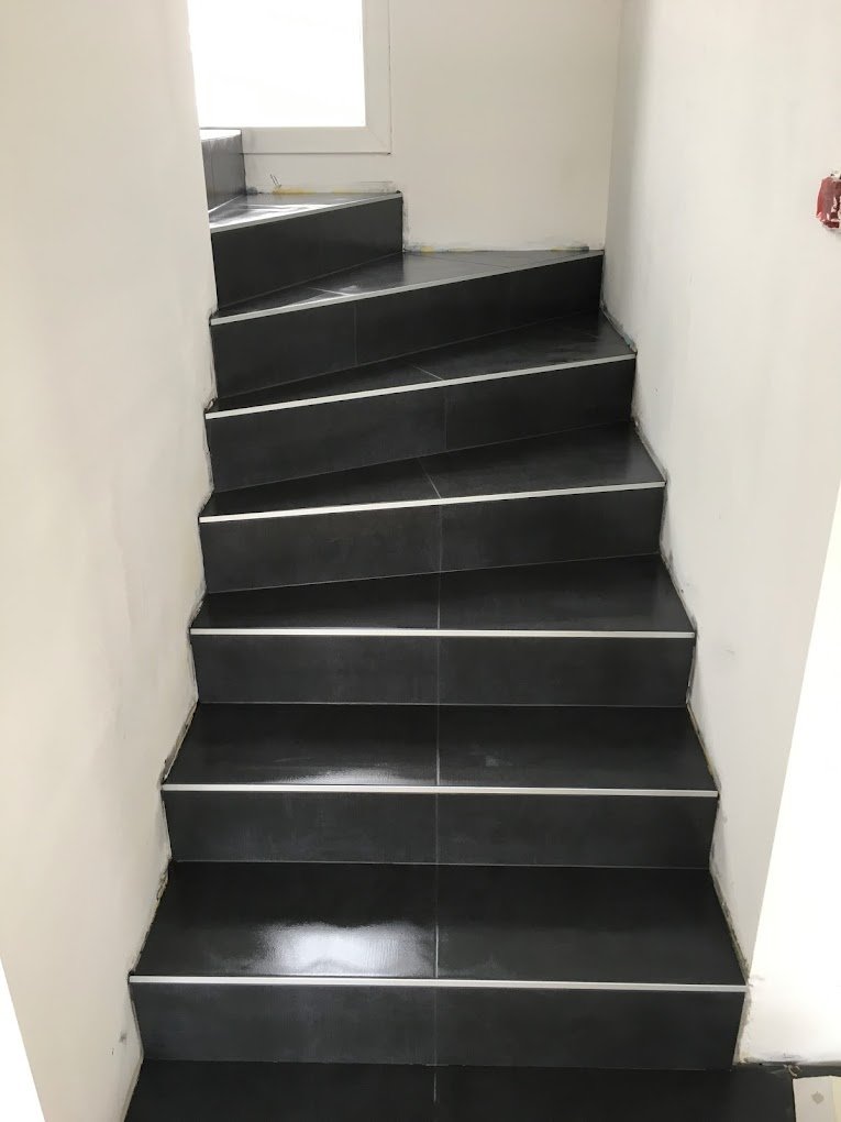 Habillage d'un escalier tournant en carrelage noir moderne avec finitions soignées par Arra Design à Rixheim.