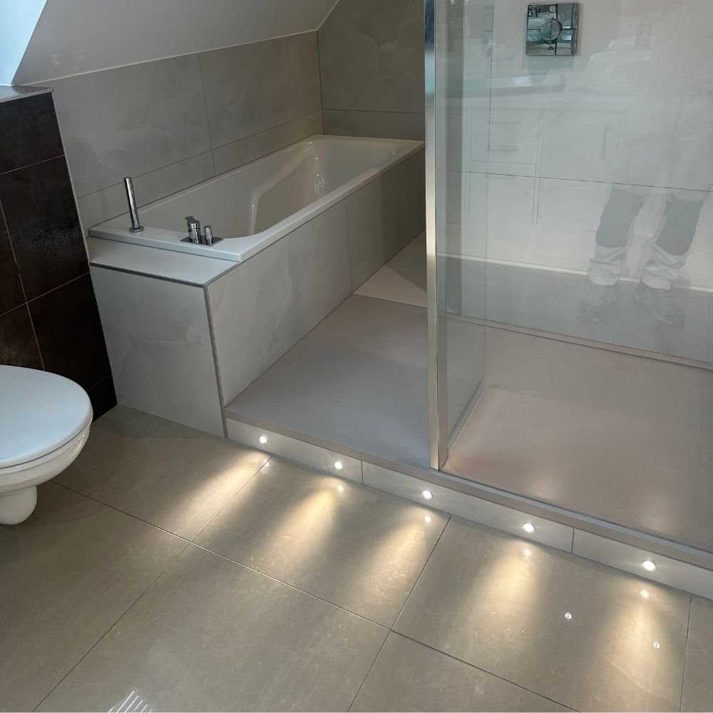 Salle de bain moderne beige avec baignoire, paroi de douche et spots LED intégrés au sol à Mulhouse.