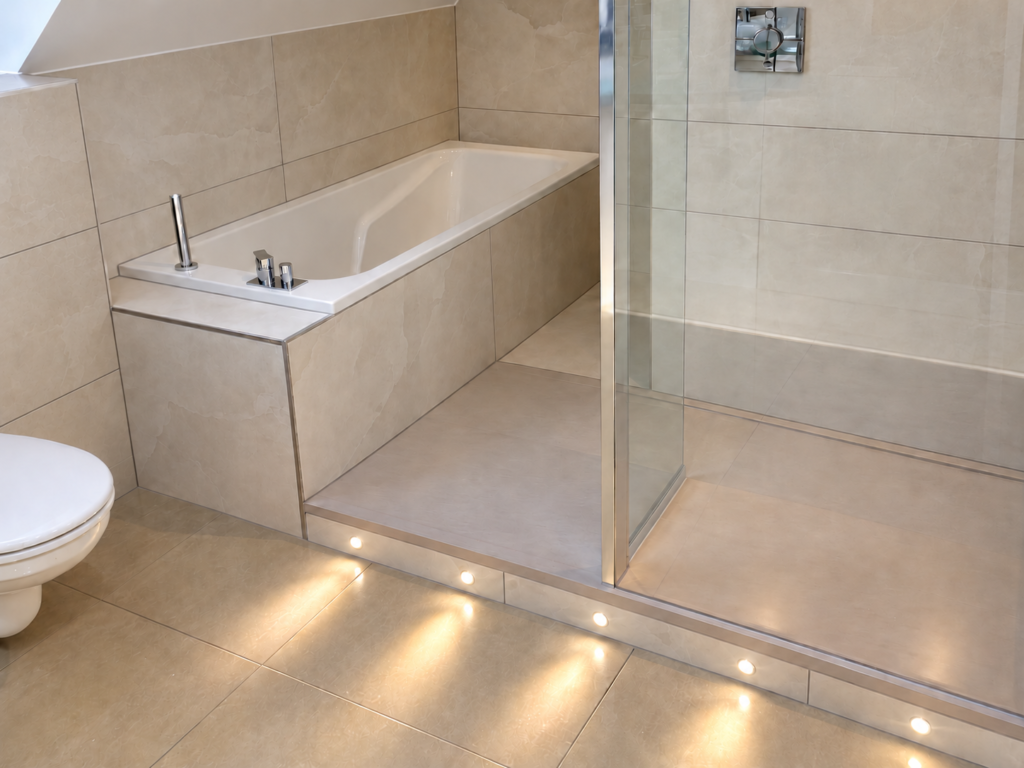 Salle de bain avec baignoire, douche vitrée, carrelage beige grand format et spots lumineux au sol
